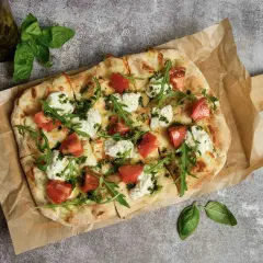 Pizza wegetariańska z pomidorami, mozzarellą i rukolą na papierze do pieczenia.