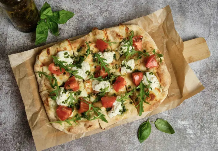 Pizza wegetariańska z pomidorami, mozzarellą i rukolą na papierze do pieczenia.