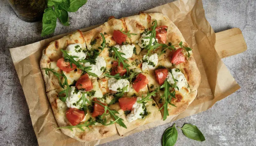 Pizza wegetariańska z pomidorami, mozzarellą i rukolą na papierze do pieczenia.
