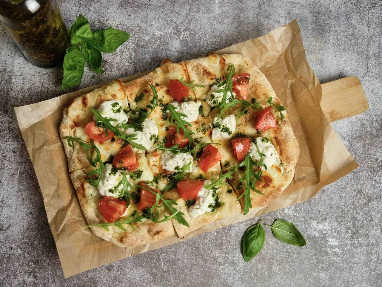 Pizza wegetariańska z pomidorami, mozzarellą i rukolą na papierze do pieczenia.